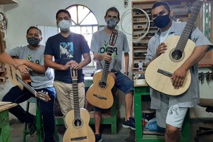 Grupo de pessoas com máscaras segurando violões em oficina.