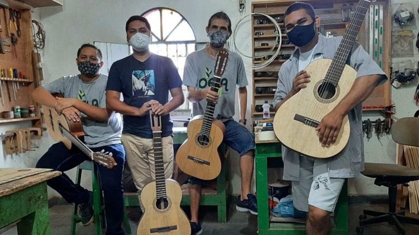 Grupo de pessoas com máscaras segurando violões em oficina.