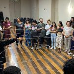 Grupo de pessoas em círculo em um workshop, com fios de barbante conectados.