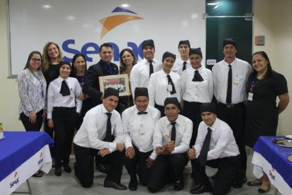 Grupo de pessoas em uniforme de garçom em frente ao logotipo da Senac