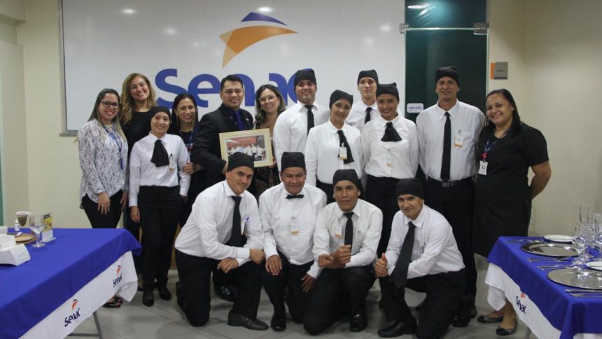 Grupo de pessoas em uniforme de garçom em frente ao logotipo da Senac