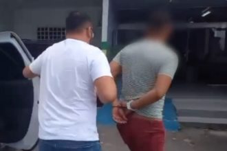 Homem é preso por estupro de vulnerável. Policial conduz suspeito algemado.