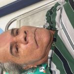 Homem idoso aguardando em hospital, usando camisa listrada