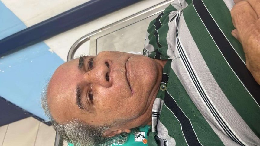 Homem idoso aguardando em hospital, usando camisa listrada
