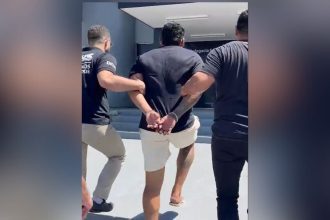 Homem preso sendo escoltado por policiais civis em frente a delegacia