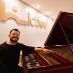 Homem sorrindo ao lado de cravo, instrumento musical barroco, no ICBEU Manaus.
