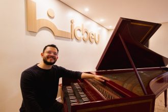 Homem sorrindo ao lado de cravo, instrumento musical barroco, no ICBEU Manaus.