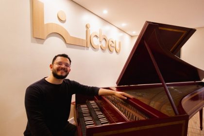 Homem sorrindo ao lado de cravo, instrumento musical barroco, no ICBEU Manaus.