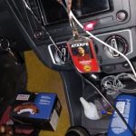 Interior de carro com chave na ignição, crachá com foto e outros objetos.