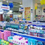 Interior de farmácia Pague Menos em Manaus, com prateleiras de produtos e banners promocionais.