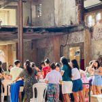 Interior de prédio antigo com pessoas em evento, possivelmente mercado. Destaca-se oficina e aula de ritmos.