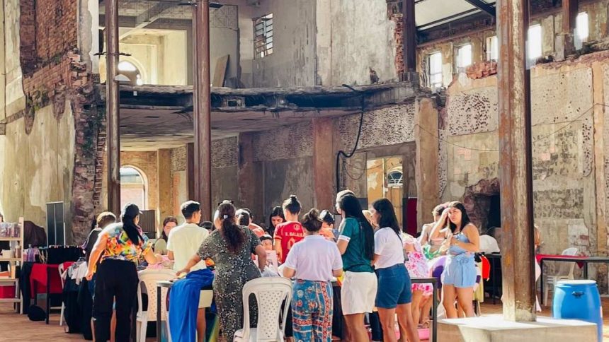 Interior de prédio antigo com pessoas em evento, possivelmente mercado. Destaca-se oficina e aula de ritmos.