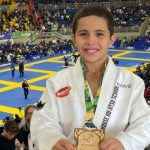 Jovem lutador de Jiu-Jitsu com medalha e troféu, em evento esportivo.