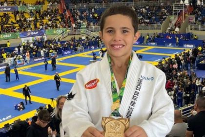 Jovem lutador de Jiu-Jitsu com medalha e troféu, em evento esportivo.