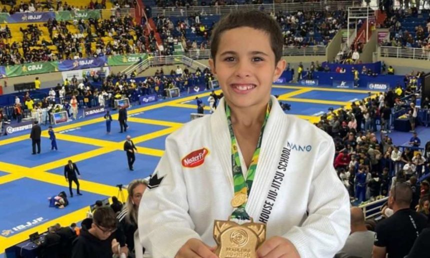 Jovem lutador de Jiu-Jitsu com medalha e troféu, em evento esportivo.