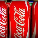 Latas de Coca-Cola vermelhas e brancas em exibição, prontas para consumo.