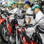 Linha de montagem de motocicletas Honda em fábrica, trabalhadores uniformizados inspecionando motos.