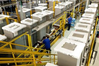 Linha de produção industrial da Electrolux em Manaus, com funcionários trabalhando.