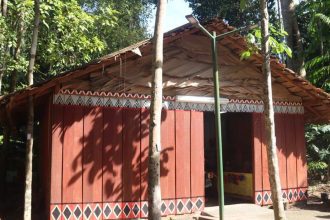 Maloca indígena no Bosque da Ciência, com arquitetura tradicional e elementos decorativos.