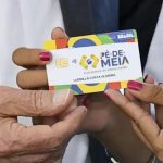 Mãos segurando cartão do programa Pé-de-Meia, com detalhes do design e informações.