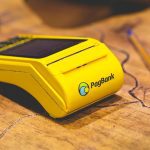 Máquina de cartão PagBank amarela sobre uma mesa de madeira.