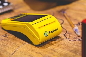 Máquina de cartão PagBank amarela sobre uma mesa de madeira.