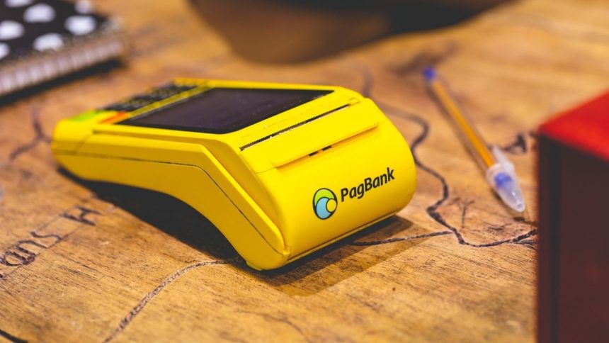 Máquina de cartão PagBank amarela sobre uma mesa de madeira.