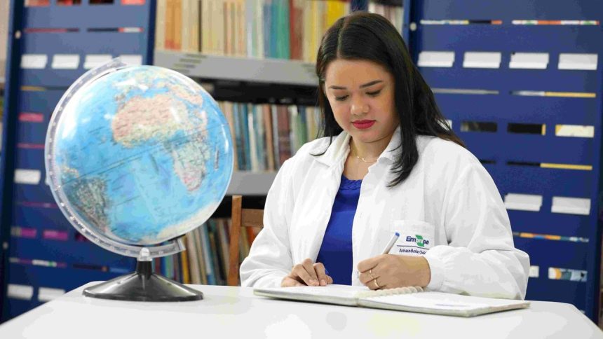 Mulher escrevendo em caderno com globo terrestre e estante de livros ao fundo.