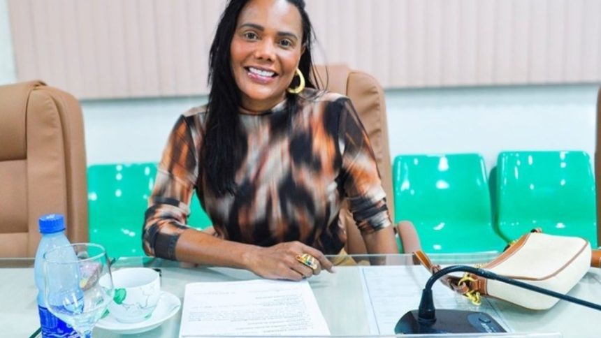 Mulher sorrindo em uma reunião, usando blusa estampada e brincos dourados.