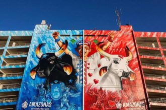 Mural colorido em edifício com bois e figuras festivas, representando o Festival de Parintins.