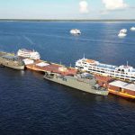 Navios atracados em uma plataforma no rio, com outros navios ao fundo.