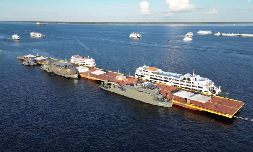 Navios atracados em uma plataforma no rio, com outros navios ao fundo.