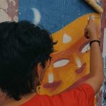 Pessoa pinta mural de lambe-lambe em exposição de arte coletiva