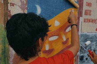 Pessoa pinta mural de lambe-lambe em exposição de arte coletiva