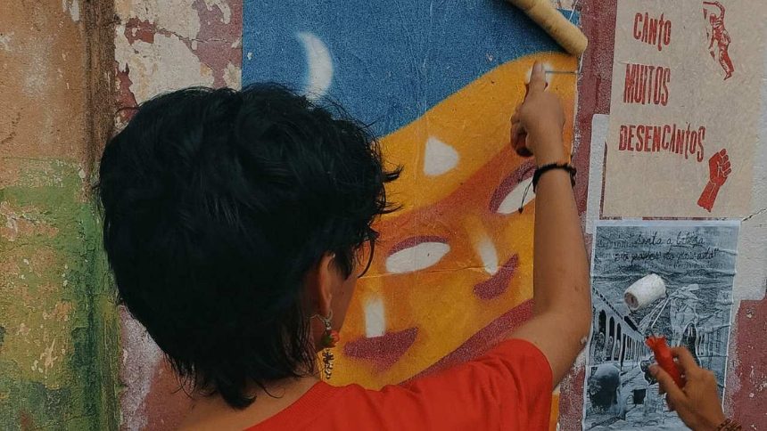 Pessoa pinta mural de lambe-lambe em exposição de arte coletiva