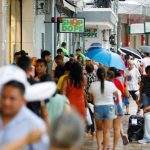Pessoas caminham em rua movimentada, possivelmente após recebimento de salário.