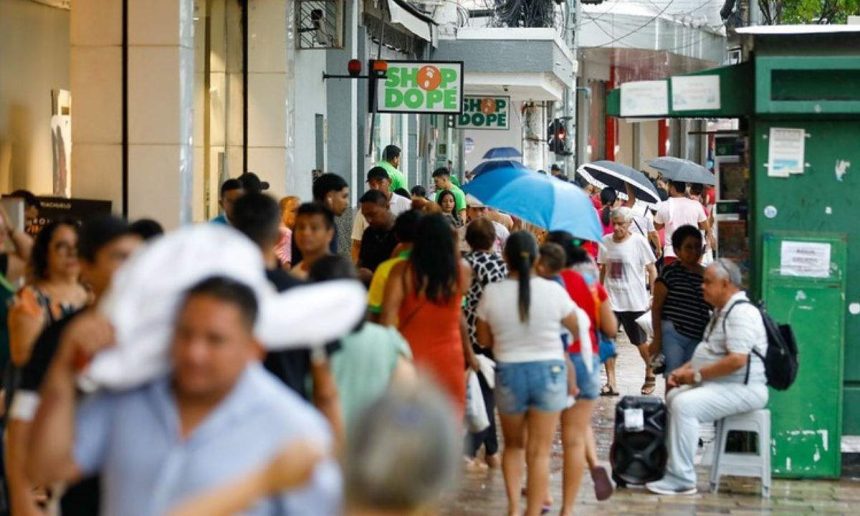Pessoas caminham em rua movimentada, possivelmente após recebimento de salário.