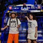 Pessoas em frente a um veículo azul, possivelmente durante evento.