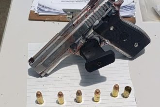 Pistola apreendida em cena de crime, com munição e vestígios de sangue.