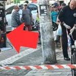 Polícia investiga cena do crime com homem morto em cadeira de rodas, com viatura e pessoas ao redor.