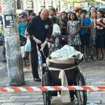 Policial em cena de crime no Centro de Manaus, cadeira de rodas e multidão observando.