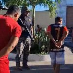 Prisão de homens após denúncia em delegacia. Policial com arma acompanha.