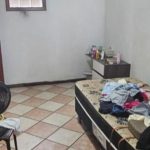 Quarto simples com roupas em cama e ventilador.