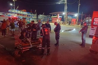 Socorristas atendem vítima de agressão em área portuária em Manaus, com ambulância e pessoas ao redor.