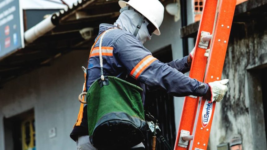 Supervisor técnico de manutenção elétrica com equipamentos de segurança e escada.