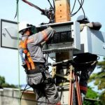 Técnicos da concessionária de energia trabalham em poste, possivelmente em manutenção ou instalação.