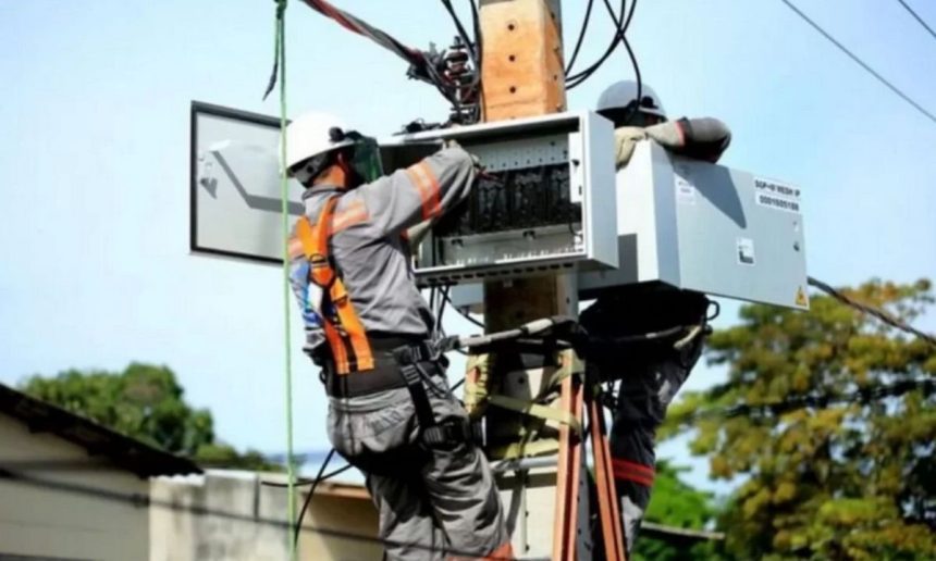 Técnicos da concessionária de energia trabalham em poste, possivelmente em manutenção ou instalação.