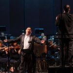 Tenor se apresenta em concerto de música clássica, com orquestra e maestro.