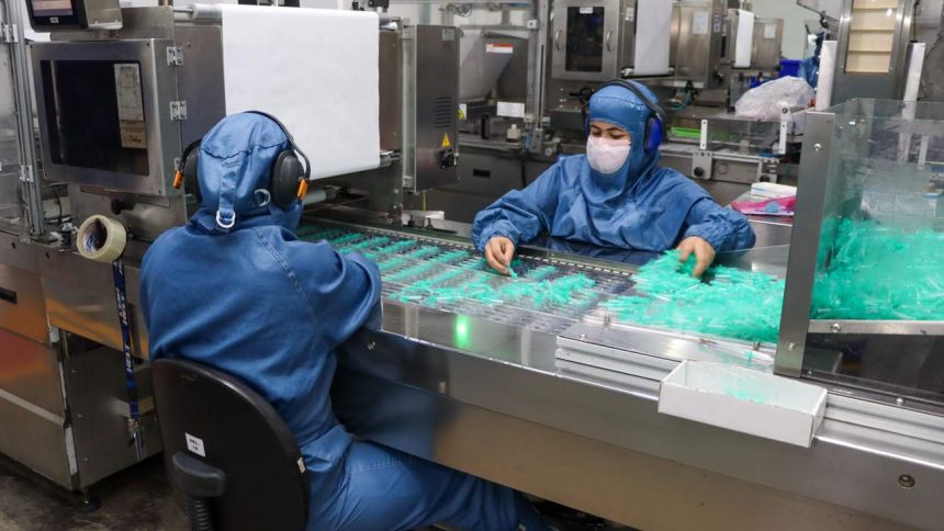 Trabalhadores em fábrica manuseando seringas em processo produtivo.