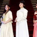 Três mulheres em trajes de época posam em frente a escadaria do Palácio da Justiça.